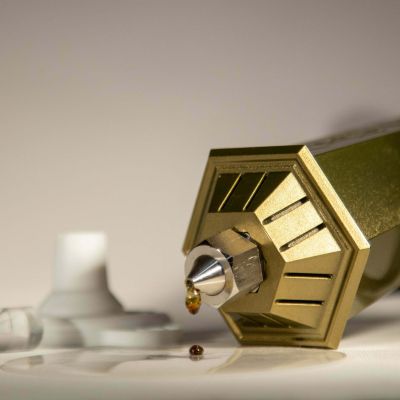 Precision-machined gold finish tip of the GEMSTX handheld rosin press dispensing a single drop of essential oil.